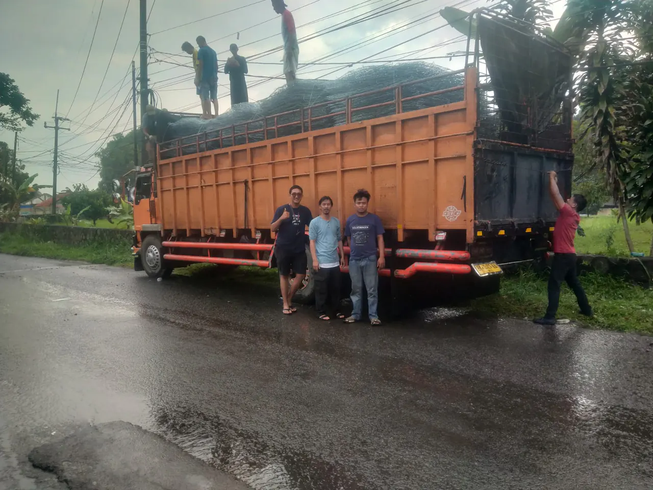 Truk bak oranye bermuatan bronjong kawat dengan awak berdiri di depannya