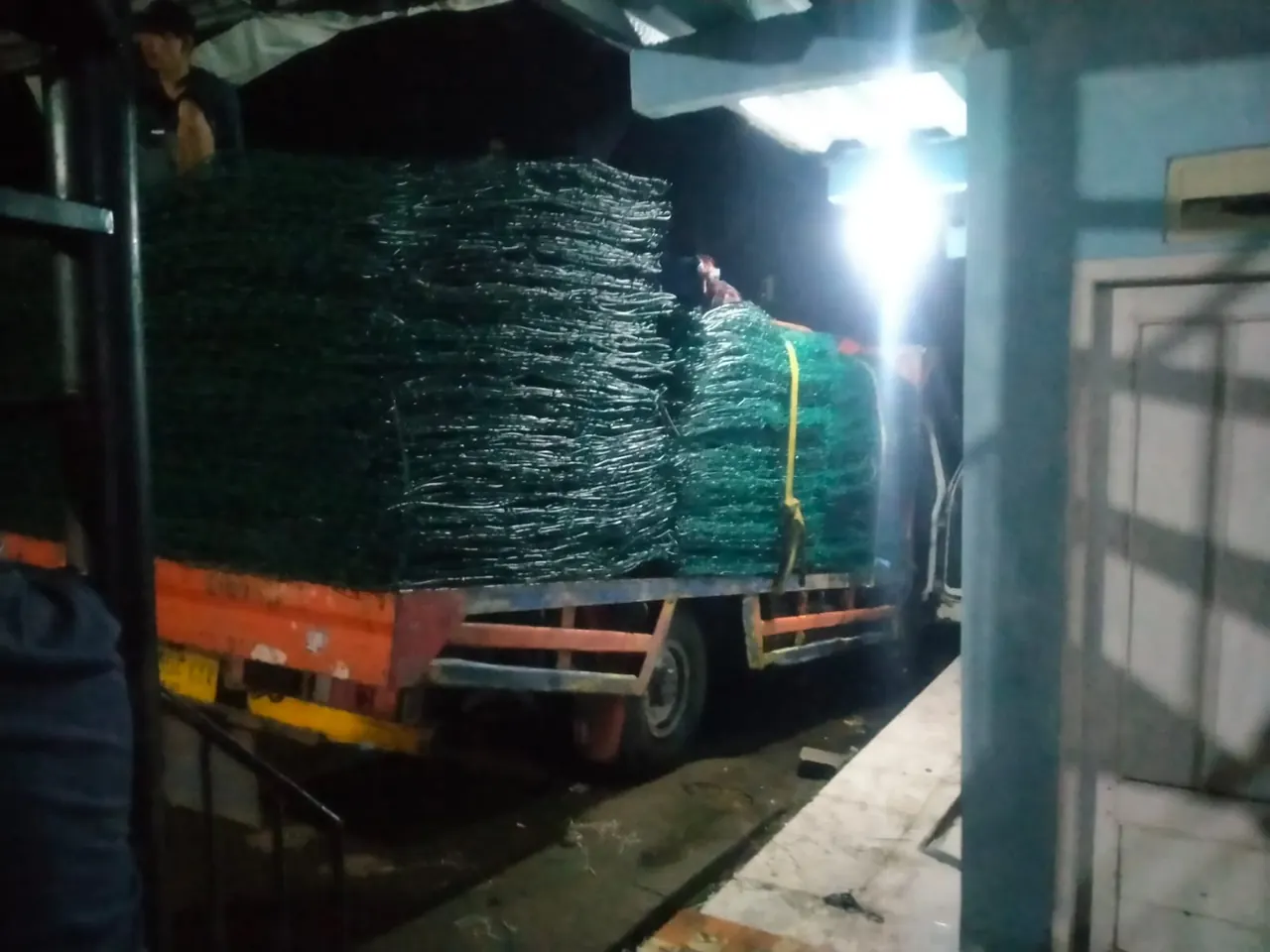Tumpukan bronjong PVC hijau di atas truk saat pengiriman malam hari