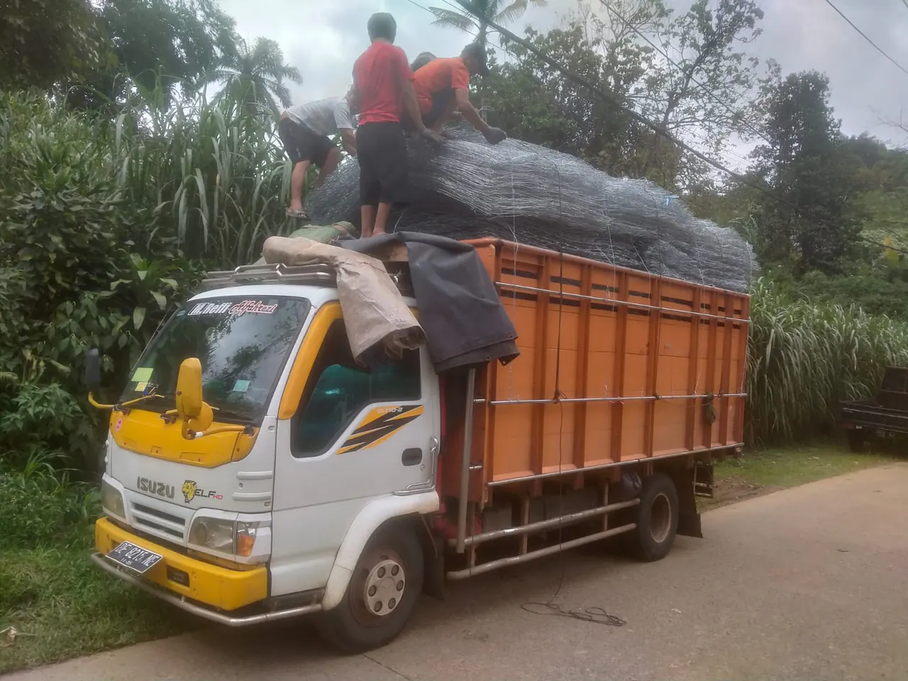 Truk putih berbak oranye mengangkut bronjong kawat