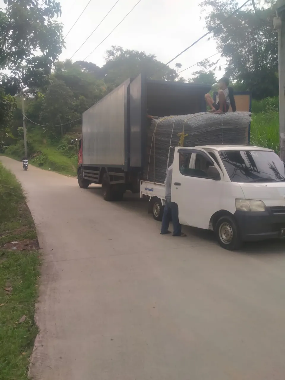 Truk box mengirim bronjong kawat melewati jalan permukiman
